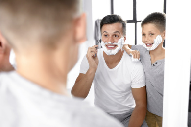 Dad showing his son how to shave near mirror in bathroom Photo of Dad showing his son how to shave near mirror in bathroom