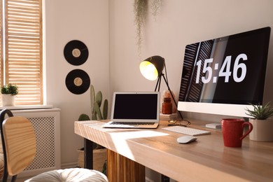 Photo of Modern computer and laptop on wooden desk in room. Interior design