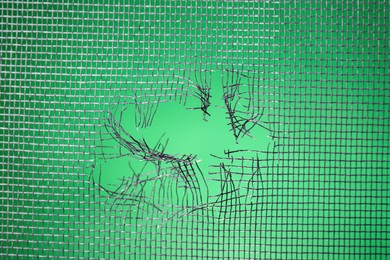 Torn window screen against green background, closeup Photo of Torn window screen against green background, closeup