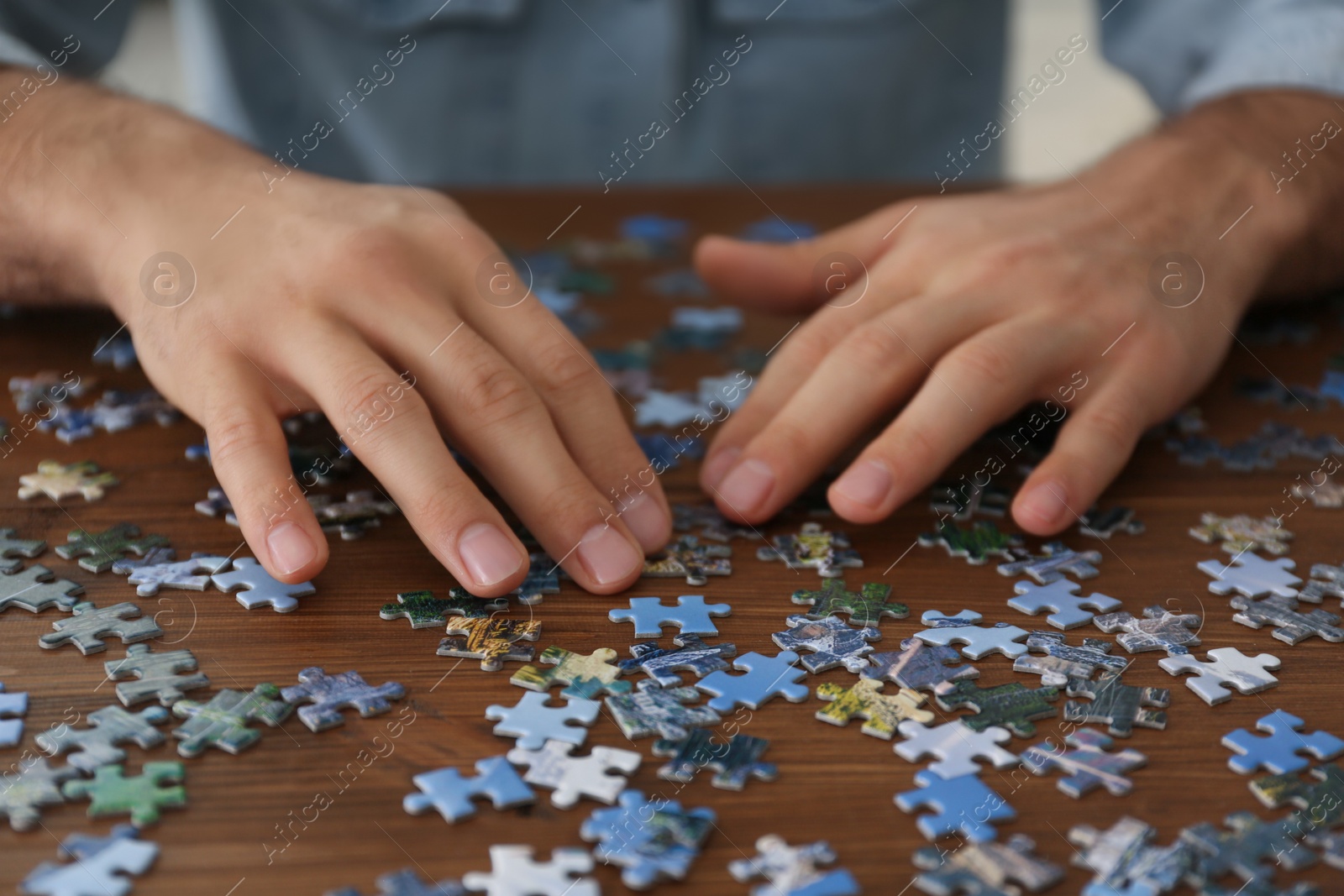 Man playing with puzzles at wooden table, closeup Photo of Man playing with puzzles at wooden table, closeup