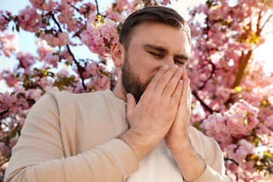 Man suffering from seasonal pollen allergy near blossoming tree outdoors Photo of Man suffering from seasonal pollen allergy near blossoming tree outdoors