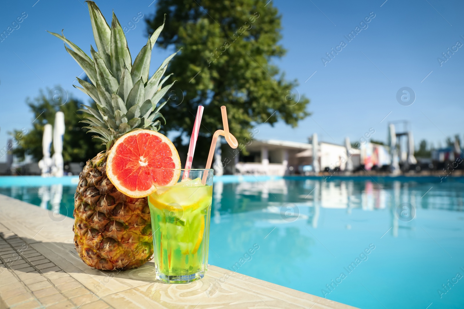 Tasty refreshing cocktail and pineapple on edge of swimming pool. Party items Photo of Tasty refreshing cocktail and pineapple on edge of swimming pool. Party items