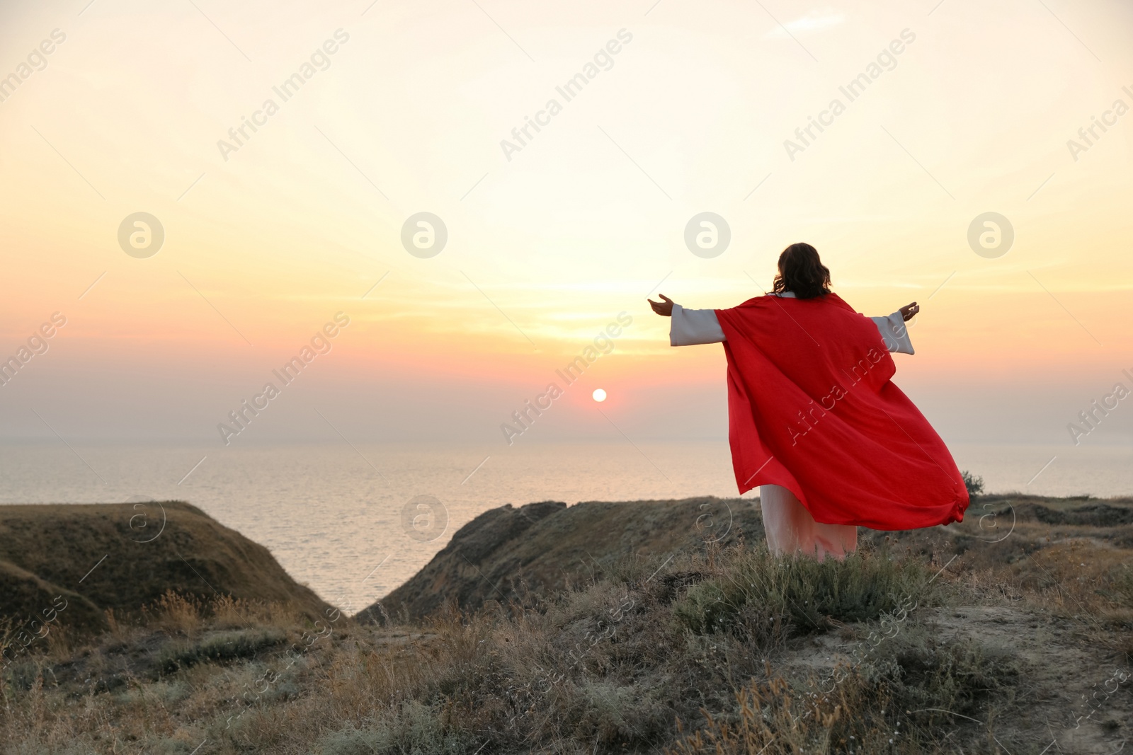 Jesus Christ raising hands on hills at sunset, back view. Space for text Photo of Jesus Christ raising hands on hills at sunset, back view. Space for text