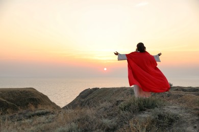 Jesus Christ raising hands on hills at sunset, back view. Space for text Photo of Jesus Christ raising hands on hills at sunset, back view. Space for text