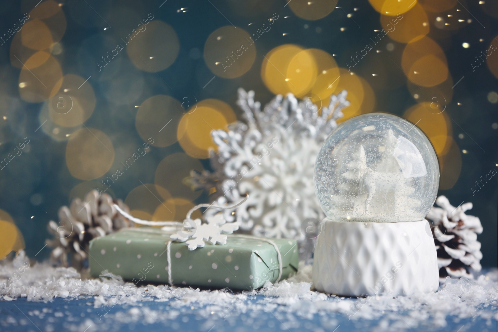 Photo of Beautiful snow globe, gift and decor on blue table against blurred Christmas lights
