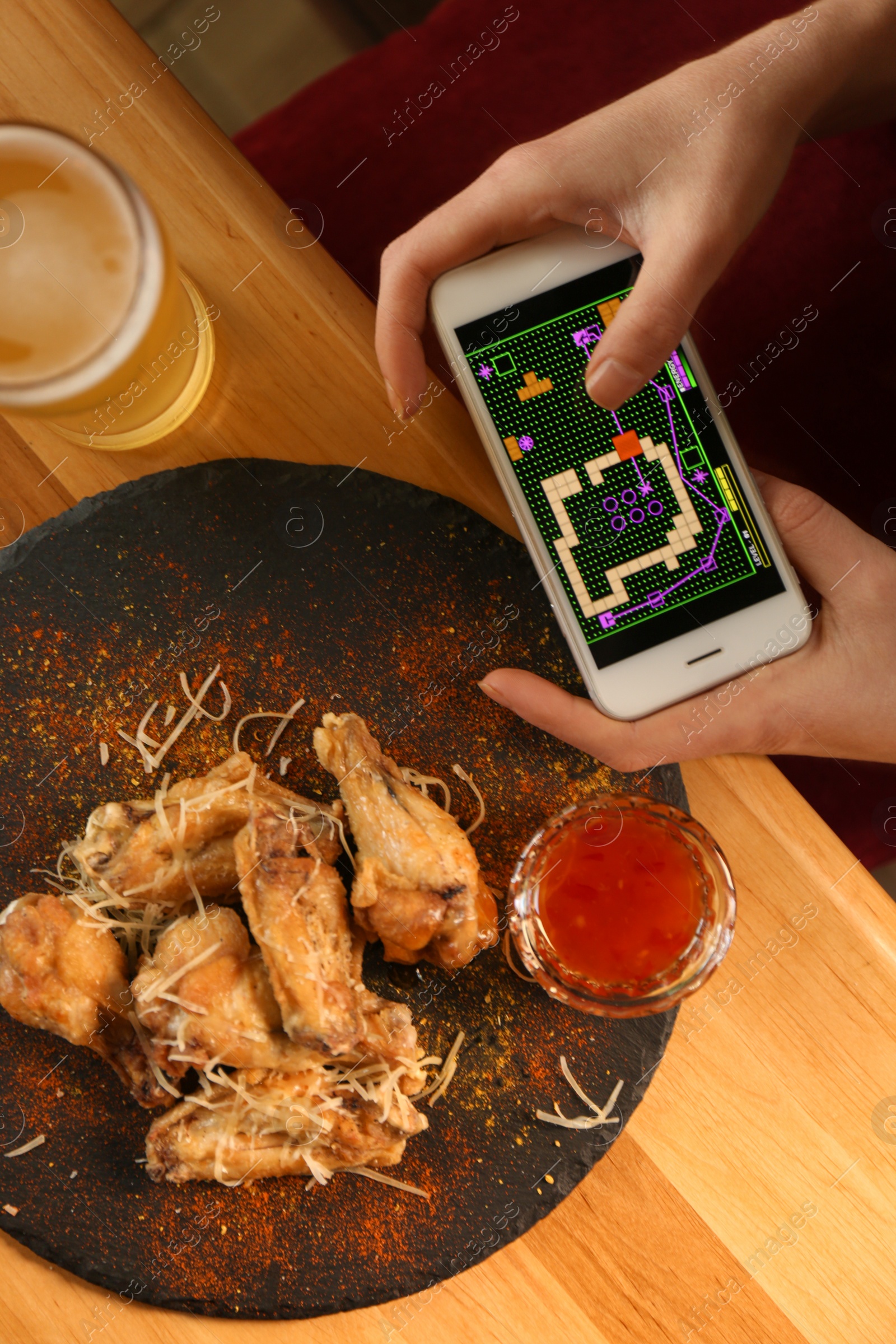 Woman playing game using smartphone at table with tasty BBQ wings, top view Photo of Woman playing game using smartphone at table with tasty BBQ wings, top view