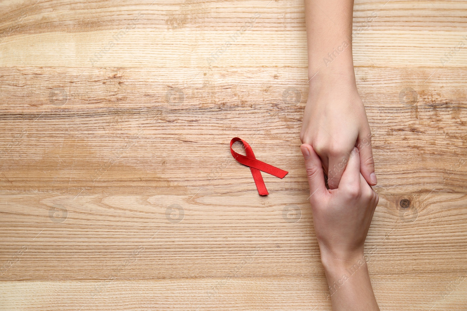 Women holding hands near red awareness ribbon on wooden background, top view with space for text. World AIDS disease day Photo of Women holding hands near red awareness ribbon on wooden background, top view with space for text. World AIDS disease day