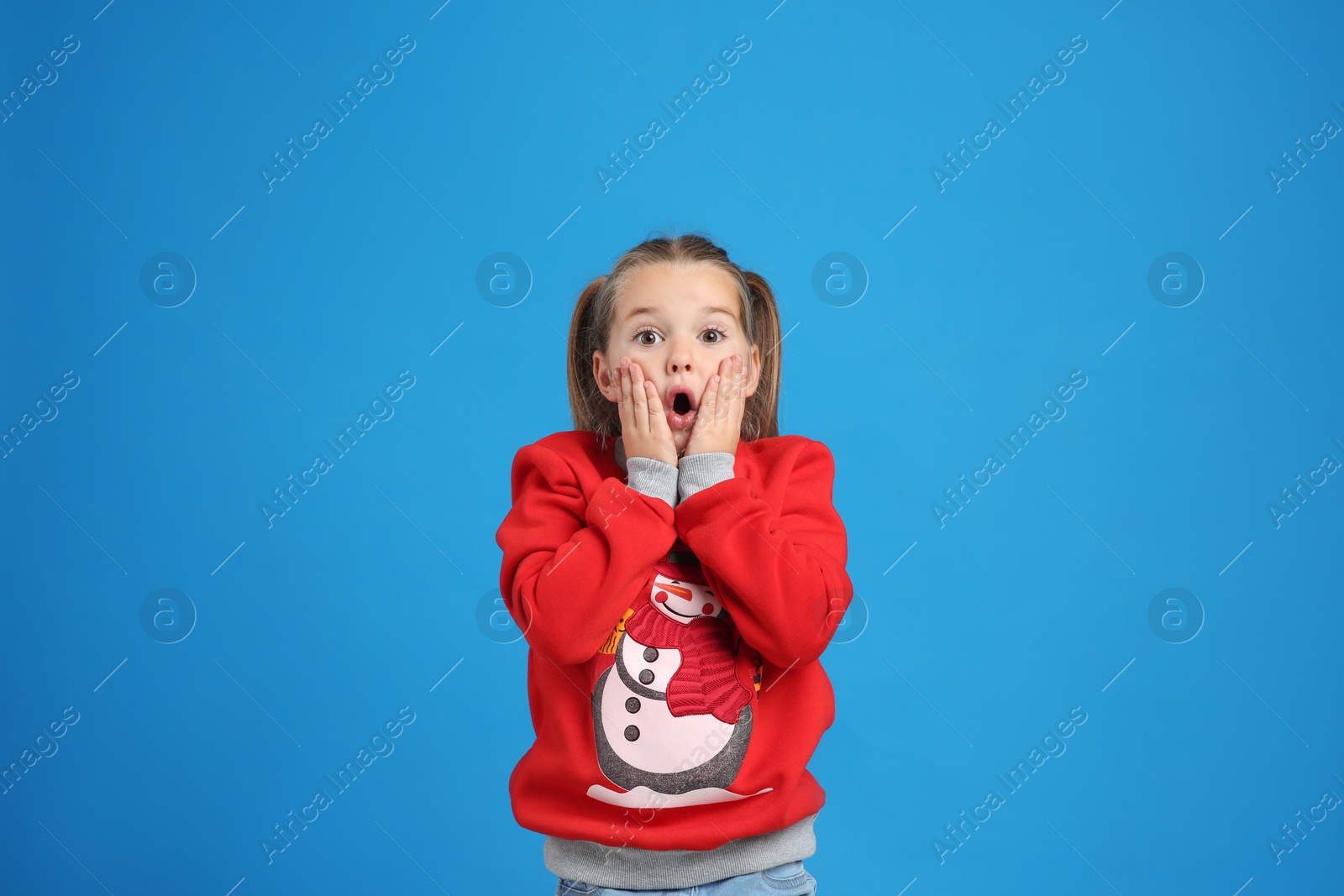 Surprised little girl in Christmas sweater on blue background Photo of Surprised little girl in Christmas sweater on blue background