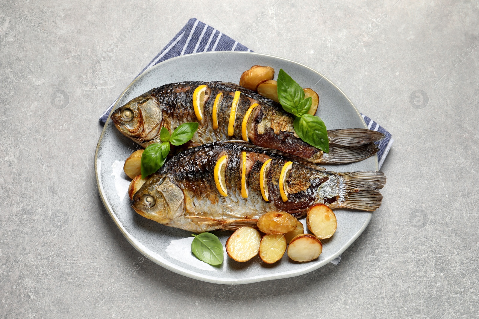 Tasty homemade roasted crucian carps with garnish on light grey table, top view. River fish Photo of Tasty homemade roasted crucian carps with garnish on light grey table, top view. River fish