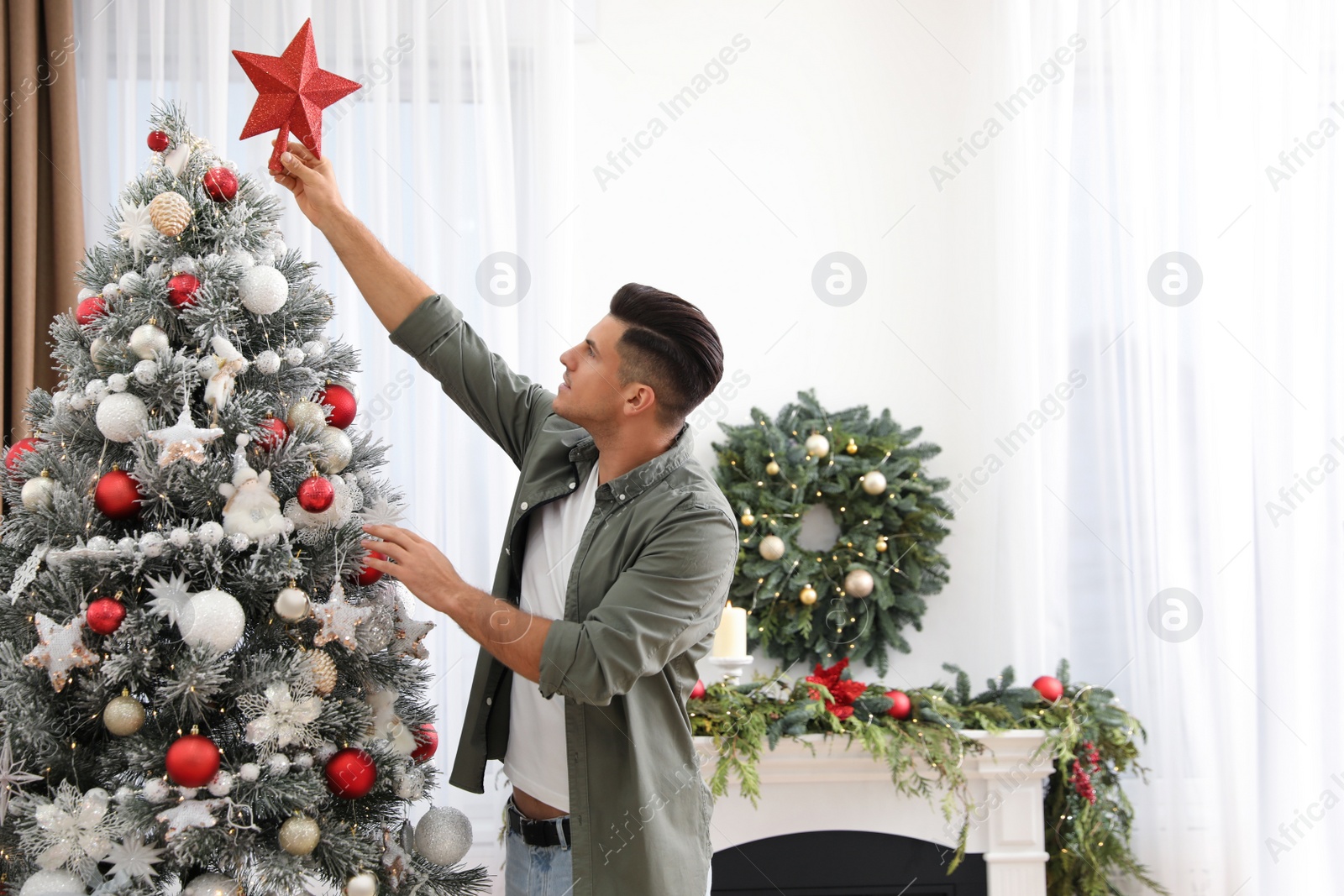 Man decorating Christmas tree with star topper indoors Photo of Man decorating Christmas tree with star topper indoors