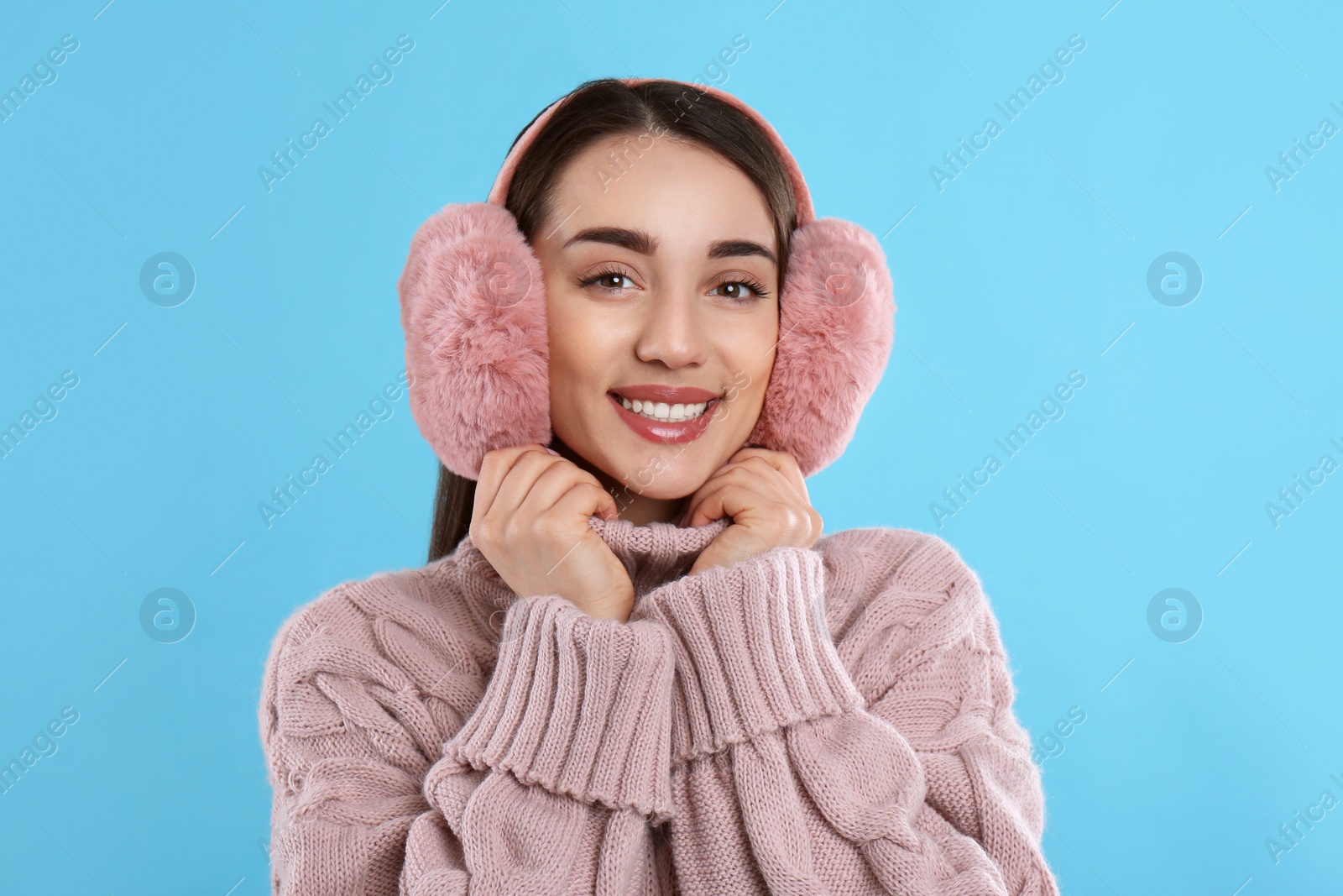 Beautiful young woman wearing earmuffs on light blue background Photo of Beautiful young woman wearing earmuffs on light blue background