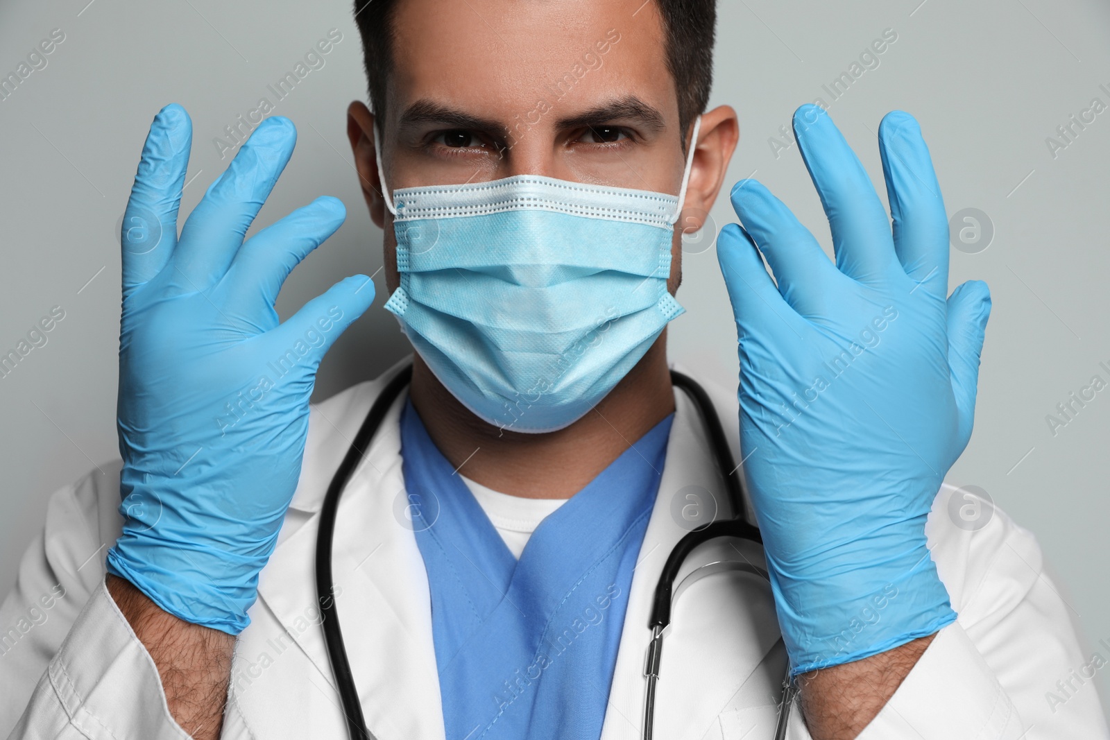 Doctor in protective mask and medical gloves against light grey background Photo of Doctor in protective mask and medical gloves against light grey background