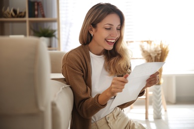 Happy woman reading letter near sofa at home Photo of Happy woman reading letter near sofa at home