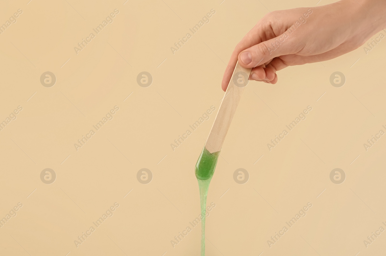 Photo of Woman holding spatula with hot depilatory wax on beige background, closeup. Space for text