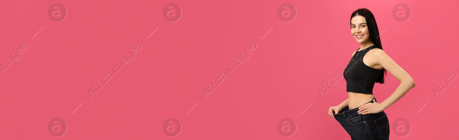 Happy young woman wearing big jeans after weight loss on pink background Photo of Happy young woman wearing big jeans after weight loss on pink background