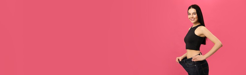 Happy young woman wearing big jeans after weight loss on pink background Photo of Happy young woman wearing big jeans after weight loss on pink background