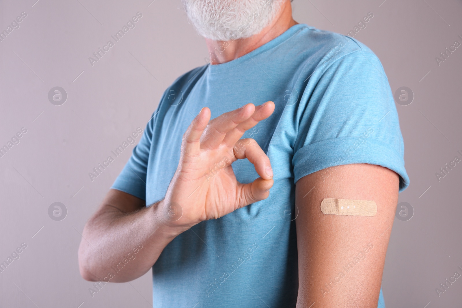 Senior man showing arm with bandage after vaccination on beige background, closeup Photo of Senior man showing arm with bandage after vaccination on beige background, closeup