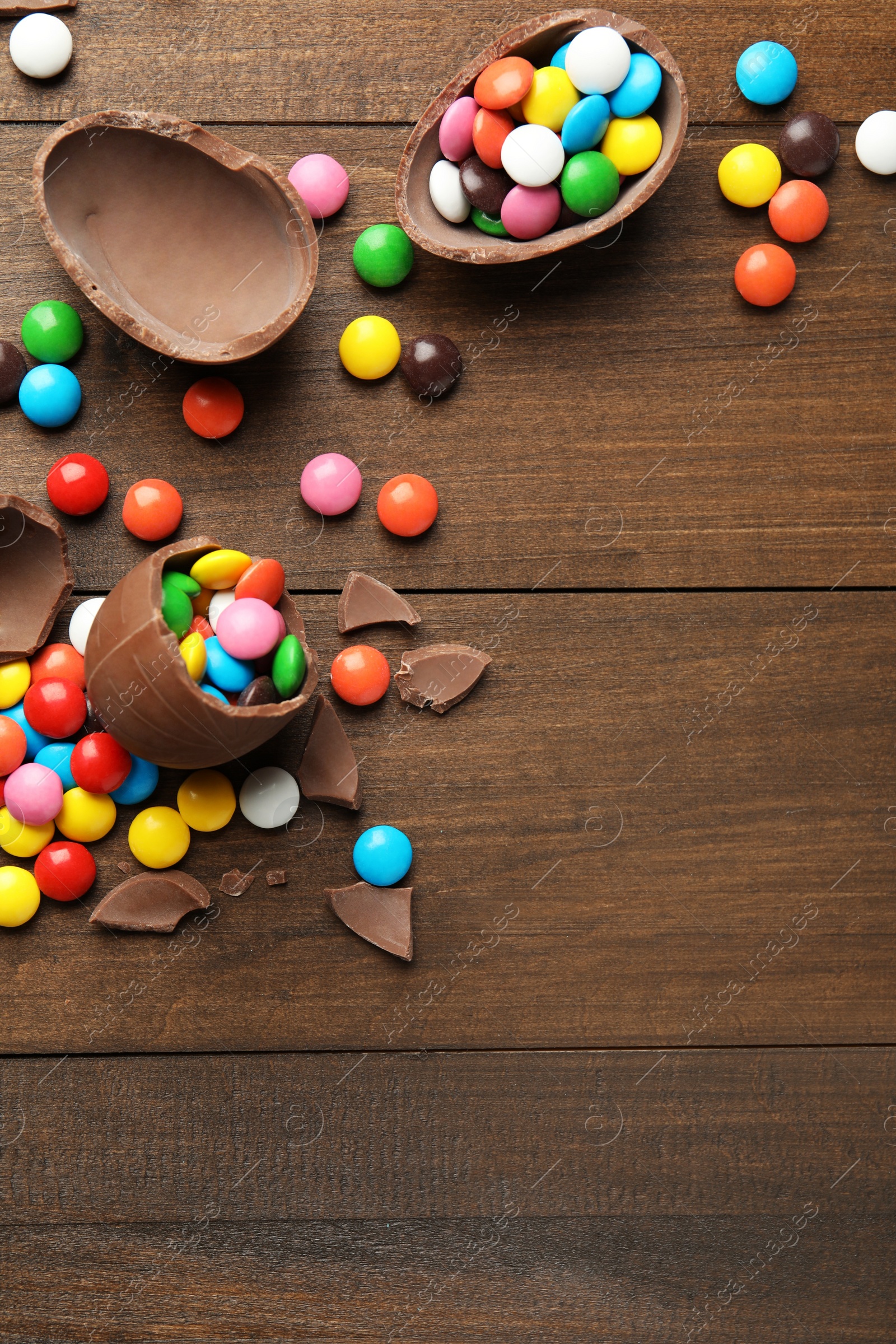 Photo of Broken chocolate eggs and colorful candies on wooden table, flat lay. Space for text