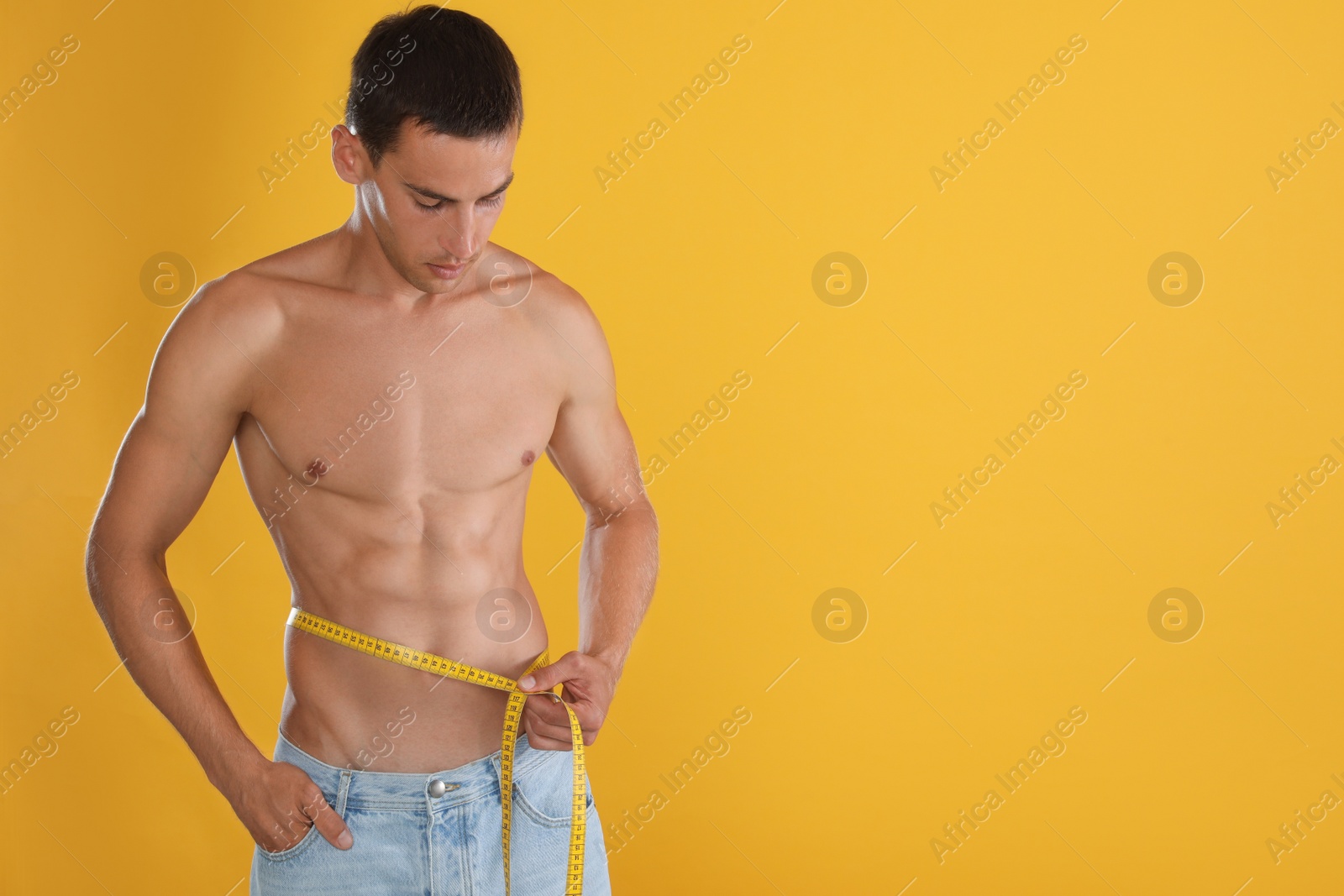 Handsome shirtless man with slim body and measuring tape around his waist on yellow background. Space for text Photo of Handsome shirtless man with slim body and measuring tape around his waist on yellow background. Space for text