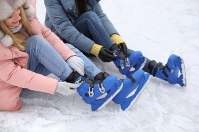 Happy women with figure skates sitting on ice rink outdoors Photo of Happy women with figure skates sitting on ice rink outdoors