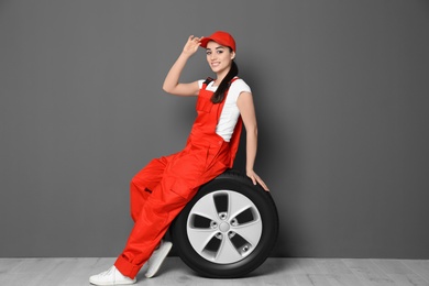 Female mechanic in uniform with car tire on grey wall background Photo of Female mechanic in uniform with car tire on grey wall background