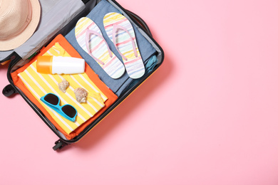 Photo of Open suitcase with beach accessories on pink background, top view. Space for text