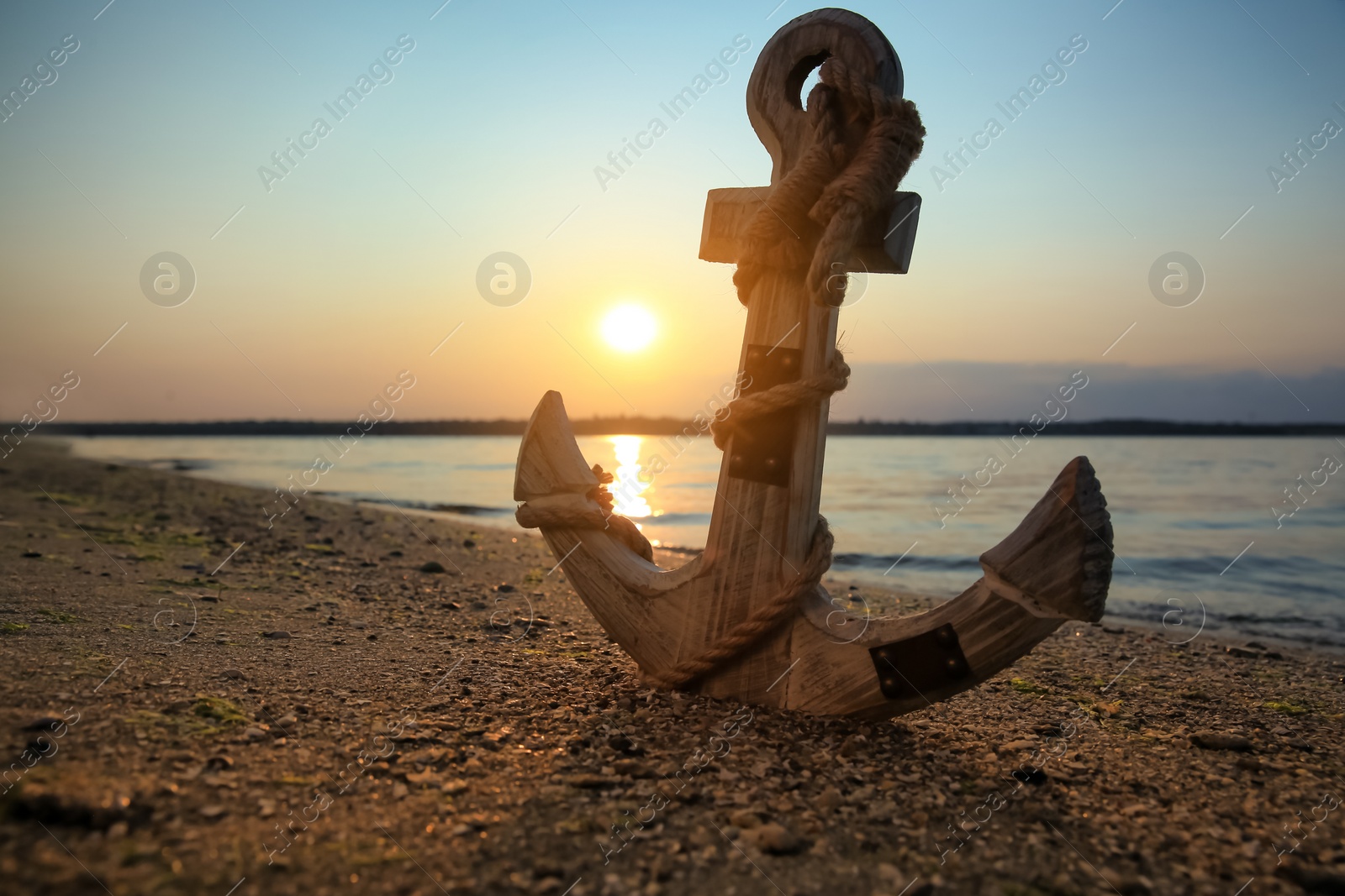 Photo of Wooden anchor on shore near river at sunset