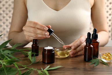 Woman dripping THC tincture or CBD oil into bowl at wooden table, closeup Photo of Woman dripping THC tincture or CBD oil into bowl at wooden table, closeup