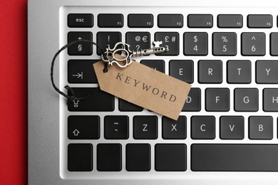 Laptop, vintage key and tag with word KEYWORD on red background, top view Photo of Laptop, vintage key and tag with word KEYWORD on red background, top view