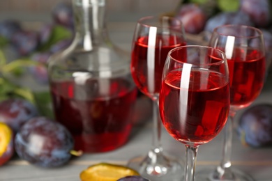 Delicious plum liquor and ripe fruits on table, closeup. Homemade strong alcoholic beverage Photo of Delicious plum liquor and ripe fruits on table, closeup. Homemade strong alcoholic beverage