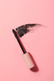 Mascara wand and smear on pink background, top view. Makeup product Photo of Mascara wand and smear on pink background, top view. Makeup product