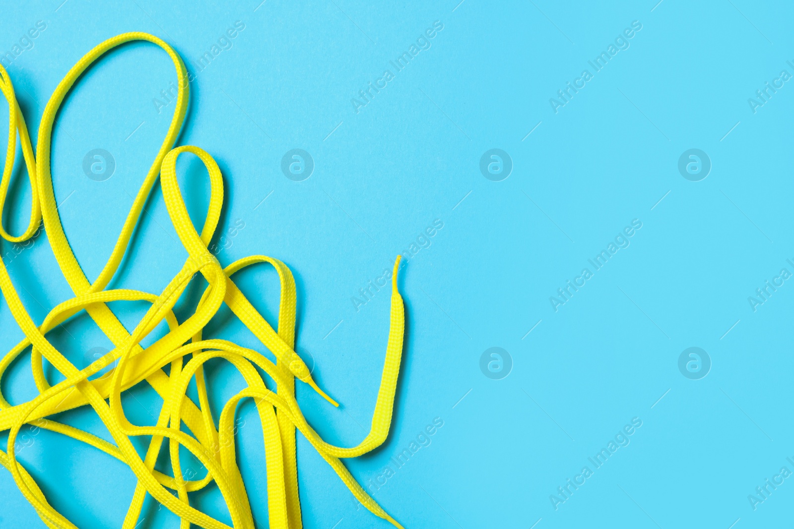 Yellow shoelaces on light blue background, flat lay. Space for text Photo of Yellow shoelaces on light blue background, flat lay. Space for text