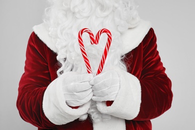 Santa Claus holding candy canes on light grey background, closeup Photo of Santa Claus holding candy canes on light grey background, closeup