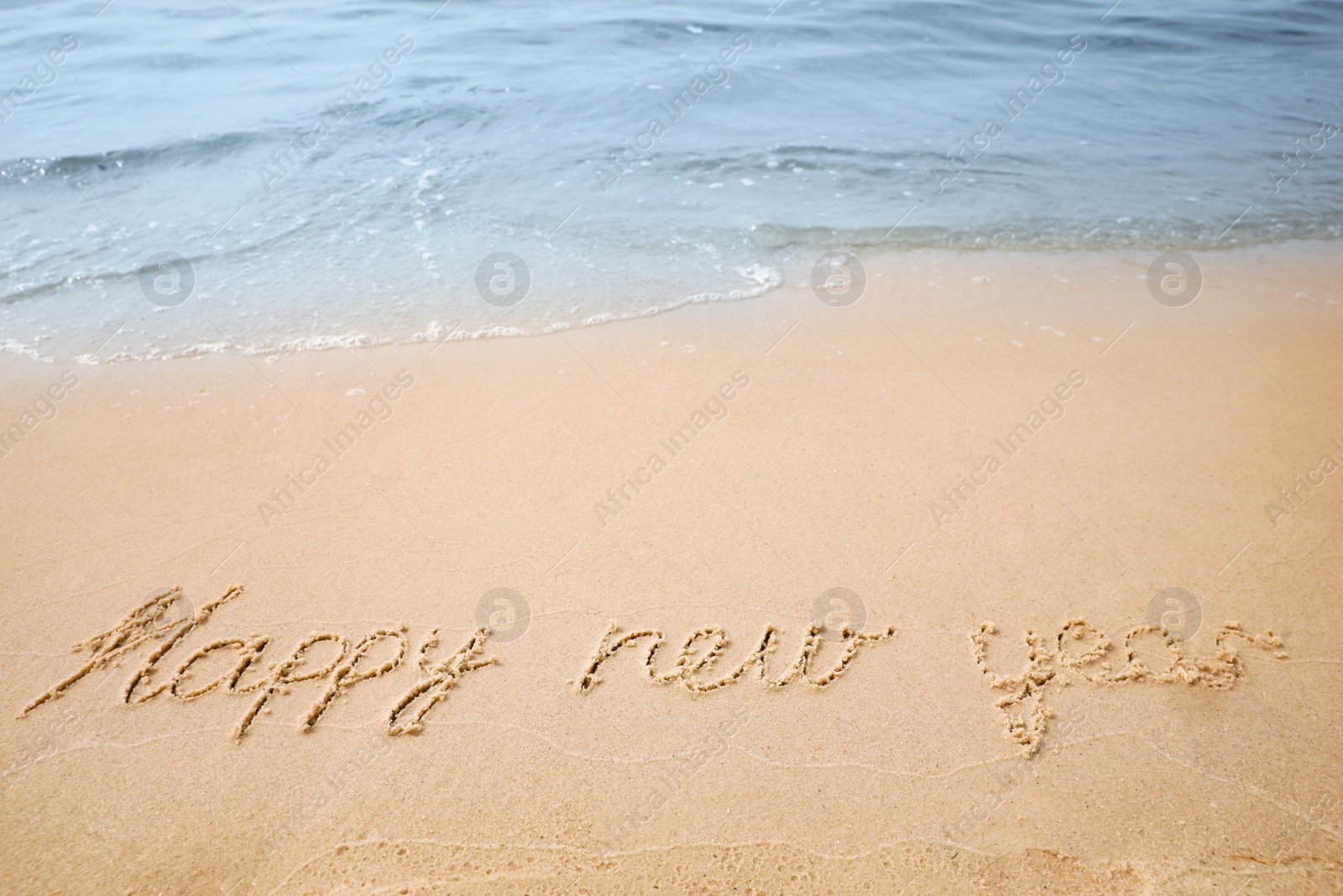 Sandy beach with text Happy New Year washed by sea Photo of Sandy beach with text Happy New Year washed by sea