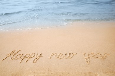 Sandy beach with text Happy New Year washed by sea Photo of Sandy beach with text Happy New Year washed by sea