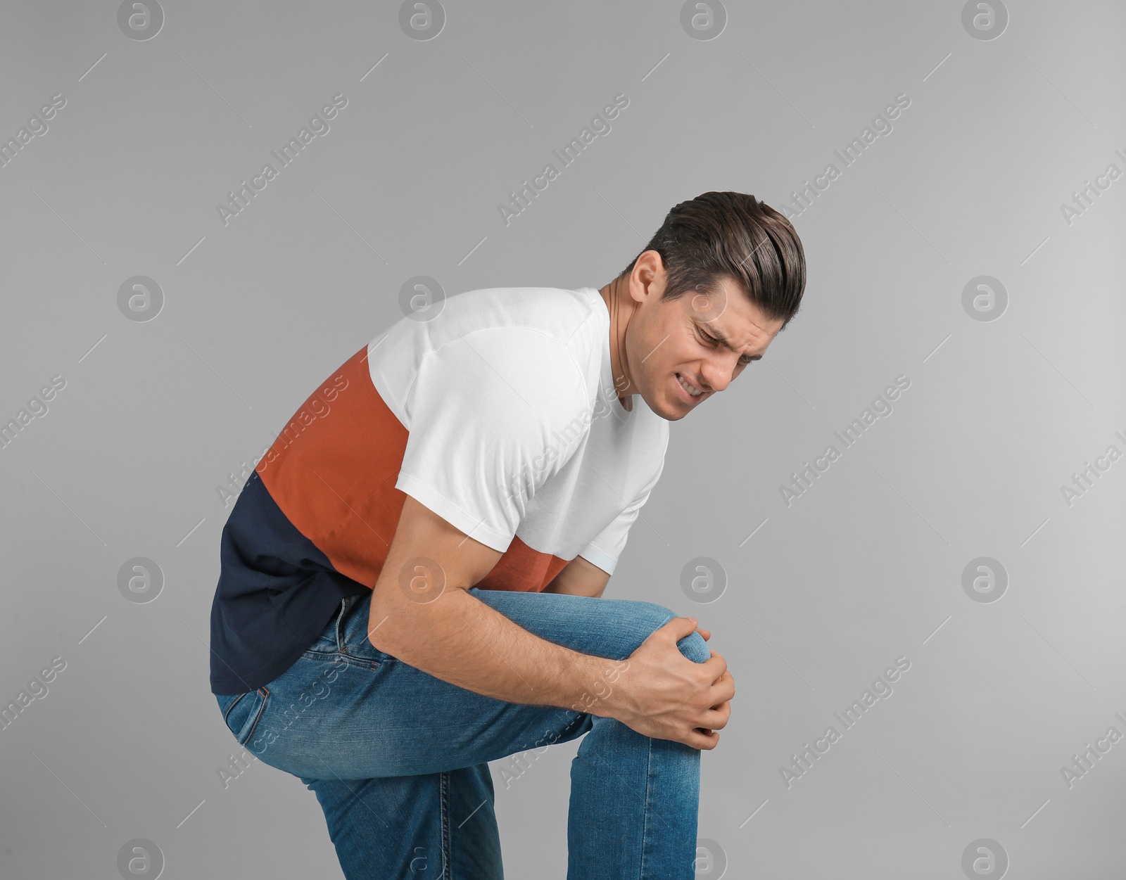 Young man suffering from knee pain on grey background Photo of Young man suffering from knee pain on grey background