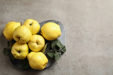 Photo of Fresh ripe organic quinces with leaves on grey table, flat lay. Space for text