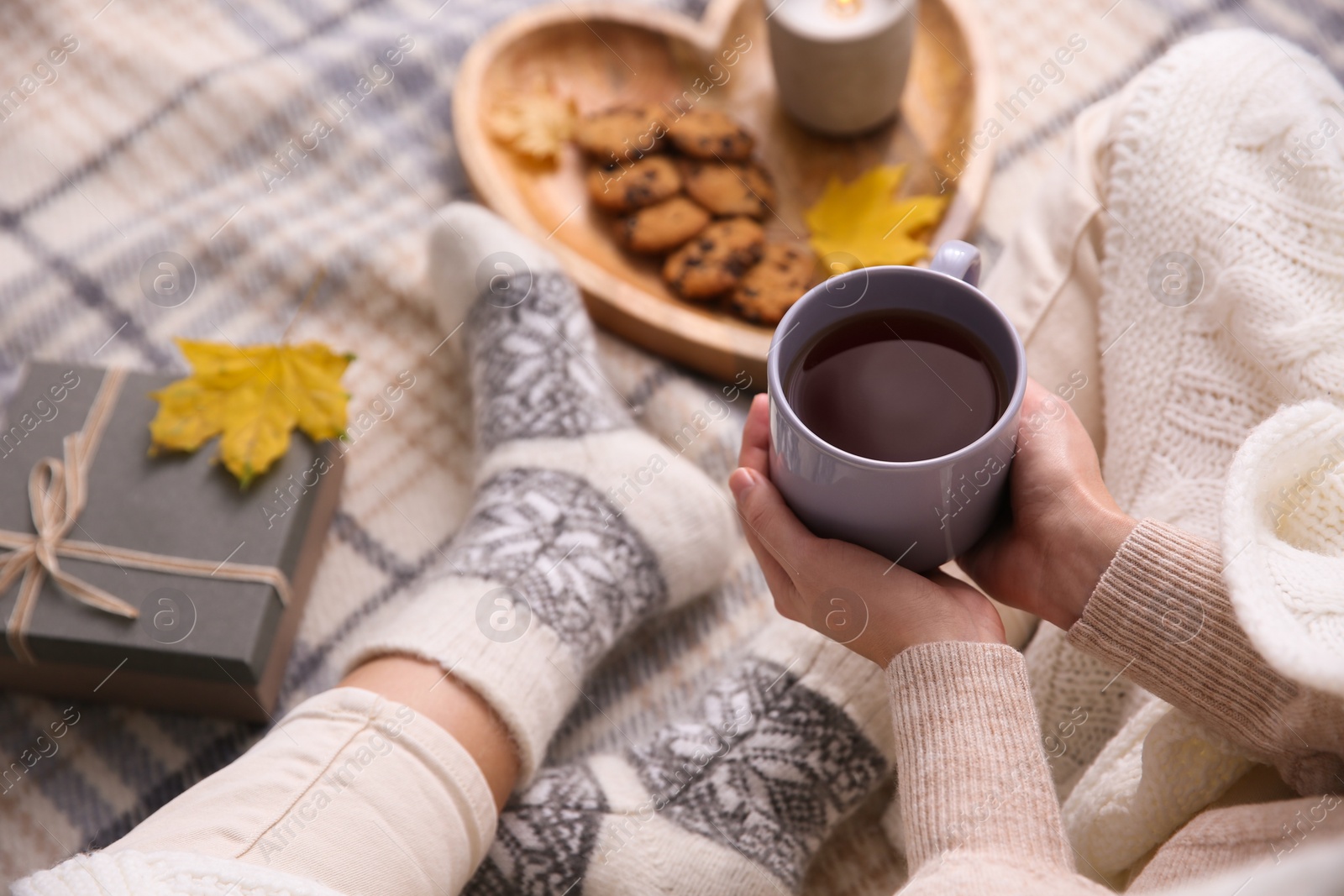 Woman relaxing with cup of hot winter drink on checkered plaid, closeup. Cozy season Photo of Woman relaxing with cup of hot winter drink on checkered plaid, closeup. Cozy season