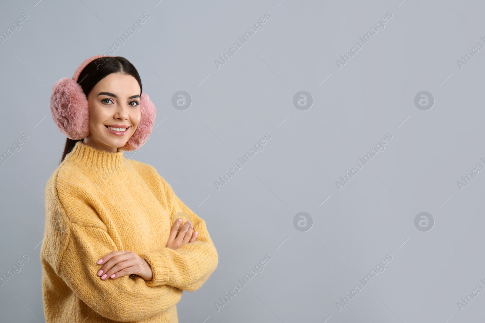 Beautiful young woman wearing earmuffs on light grey background. Space for text Photo of Beautiful young woman wearing earmuffs on light grey background. Space for text