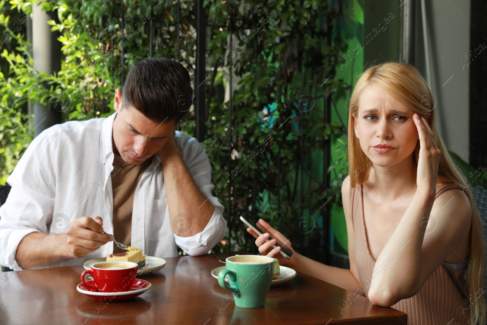 Young woman with smartphone ignoring her boyfriend in outdoor cafe. Boring date Photo of Young woman with smartphone ignoring her boyfriend in outdoor cafe. Boring date