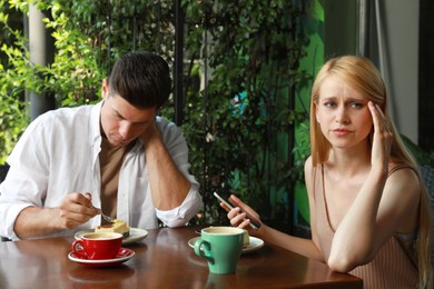 Young woman with smartphone ignoring her boyfriend in outdoor cafe. Boring date Photo of Young woman with smartphone ignoring her boyfriend in outdoor cafe. Boring date