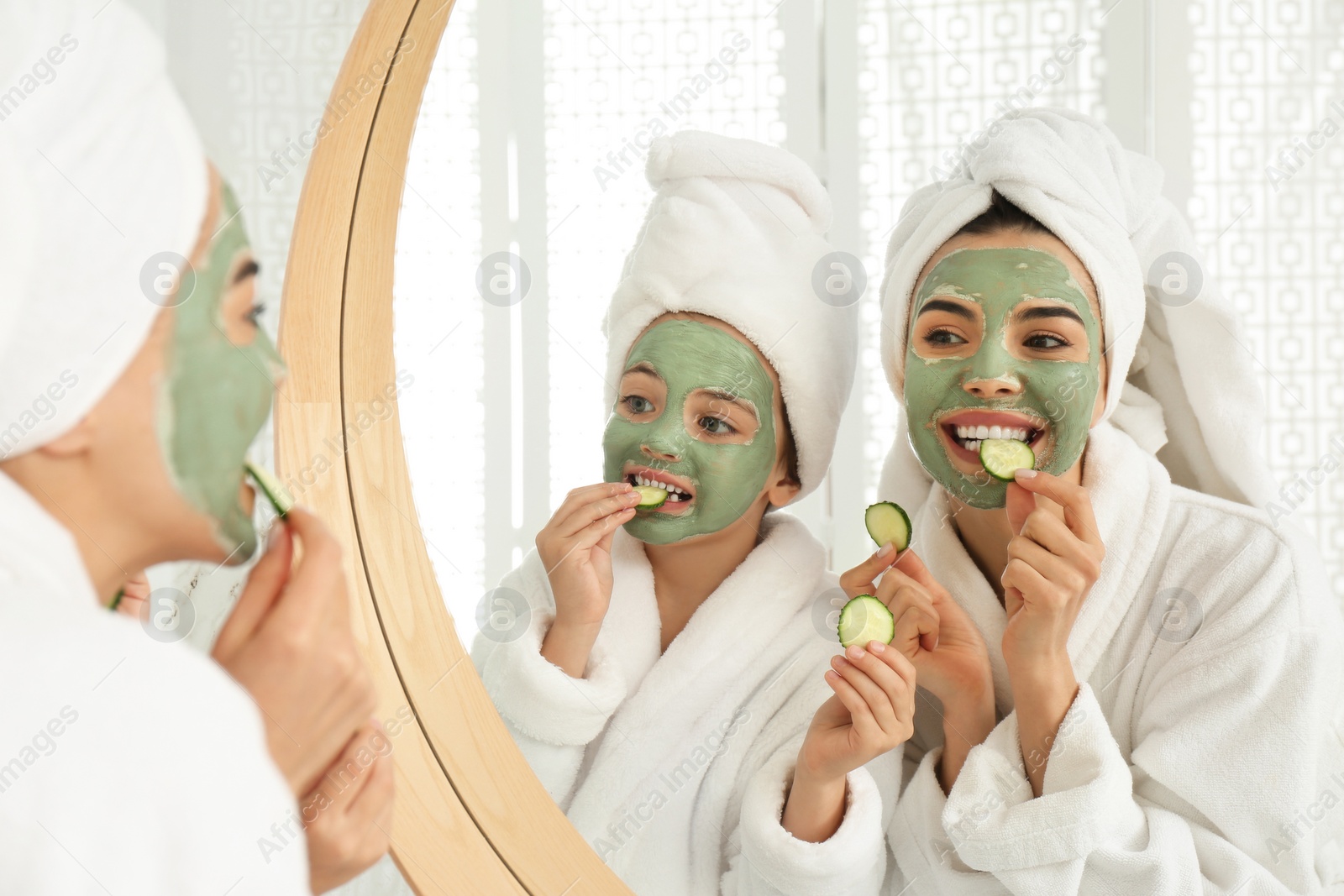 Young mother and her daughter with facial masks near mirror in bathroom Photo of Young mother and her daughter with facial masks near mirror in bathroom