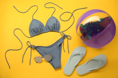 Photo of Stylish blue bikini and beach accessories on yellow background, flat lay
