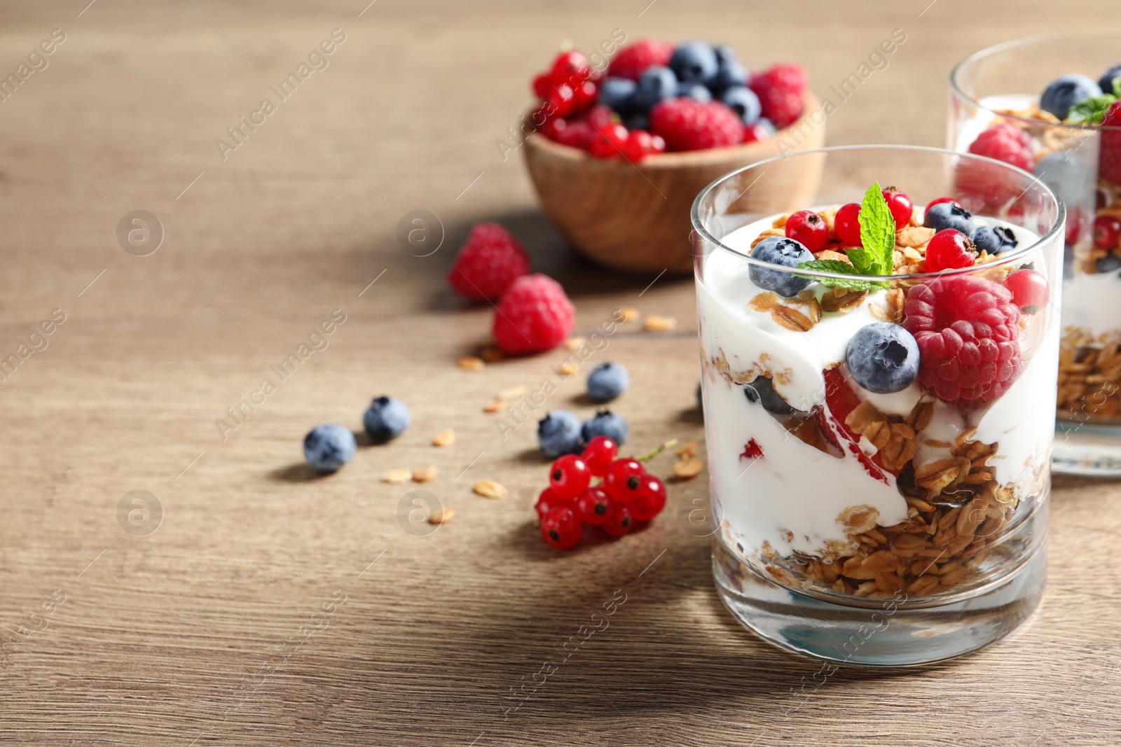 Tasty dessert with yogurt, berries and granola on wooden table. Space for text Image of Tasty dessert with yogurt, berries and granola on wooden table. Space for text