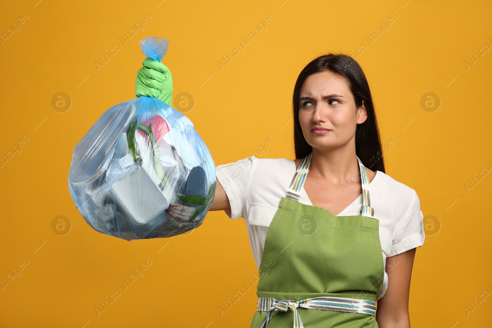 Woman holding full garbage bag on yellow background Photo of Woman holding full garbage bag on yellow background