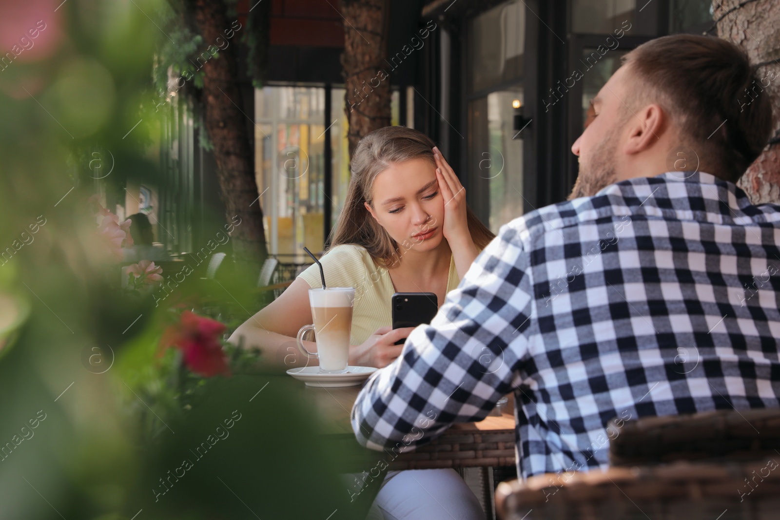 Young woman distracting herself with smartphone during boring date in outdoor cafe Photo of Young woman distracting herself with smartphone during boring date in outdoor cafe