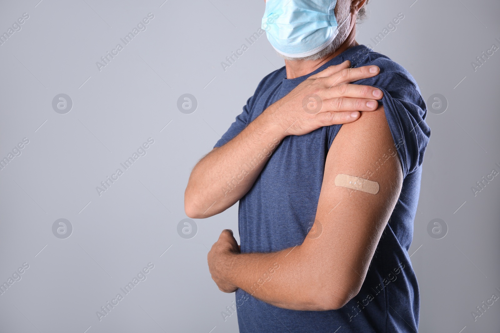 Senior man in protective mask showing arm with bandage after vaccination on grey background, closeup. Space for text Photo of Senior man in protective mask showing arm with bandage after vaccination on grey background, closeup. Space for text