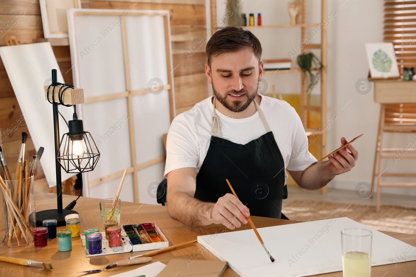 Young man painting with brush in artist studio Photo of Young man painting with brush in artist studio