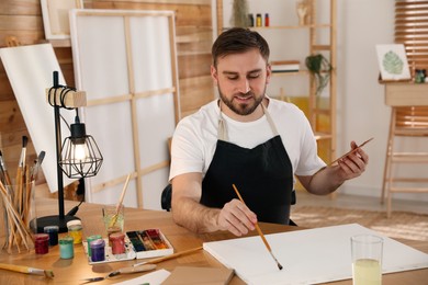 Young man painting with brush in artist studio Photo of Young man painting with brush in artist studio