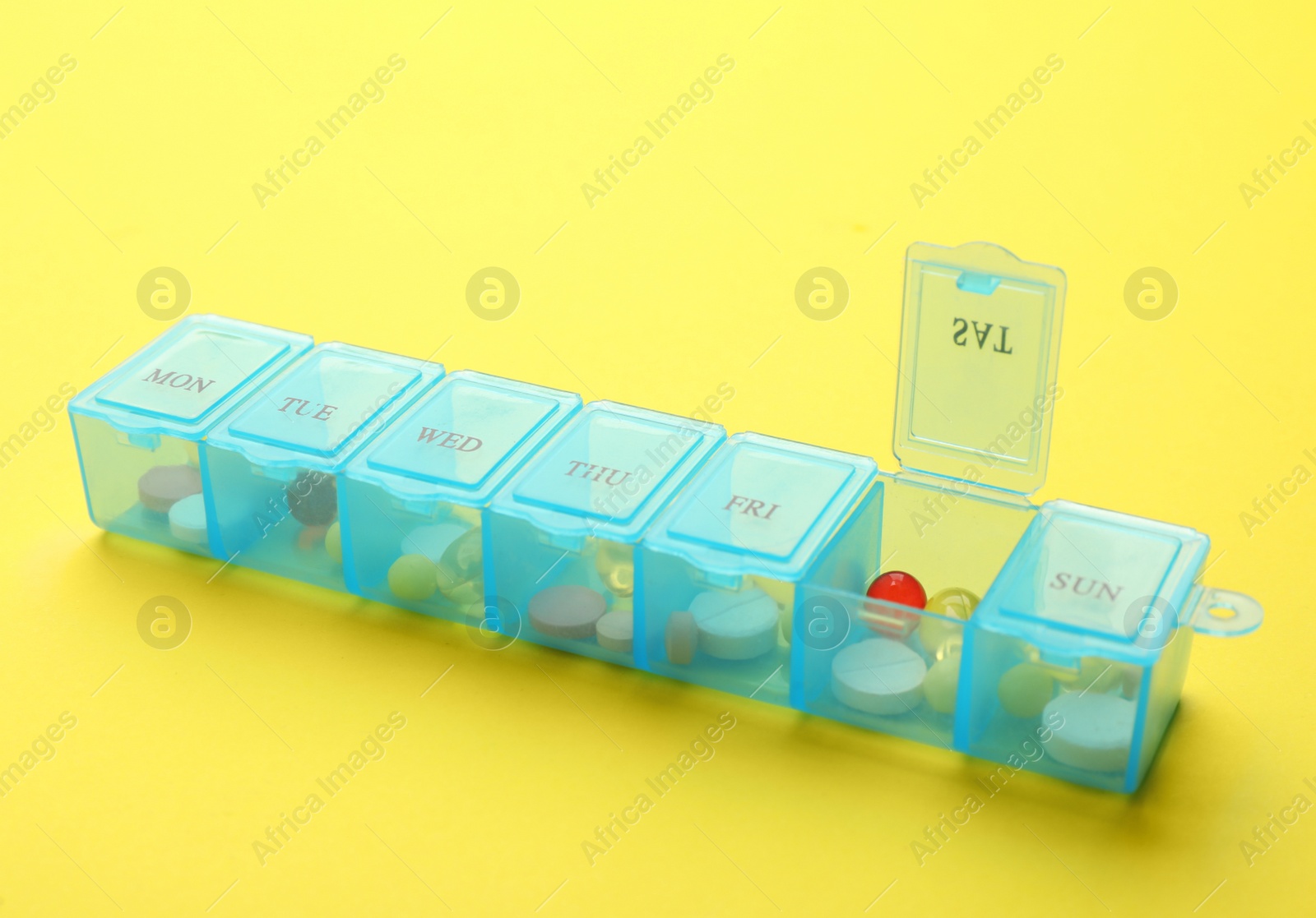 Plastic box with different pills on yellow background Photo of Plastic box with different pills on yellow background